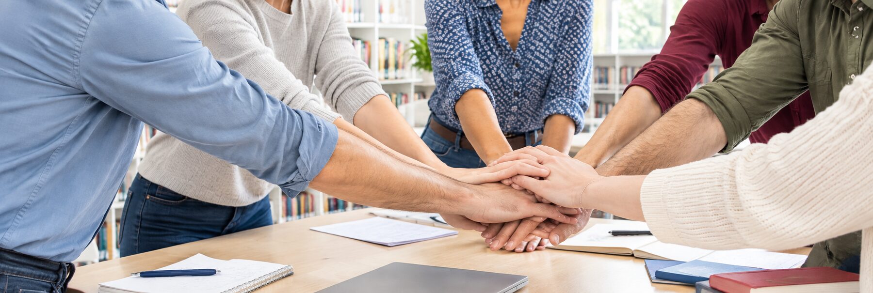 Mani di persone adulte unite al centro di un tavolo, in biblioteca